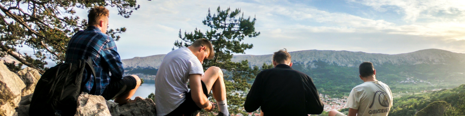 four men sit after a hike looking at the landscape of mountains